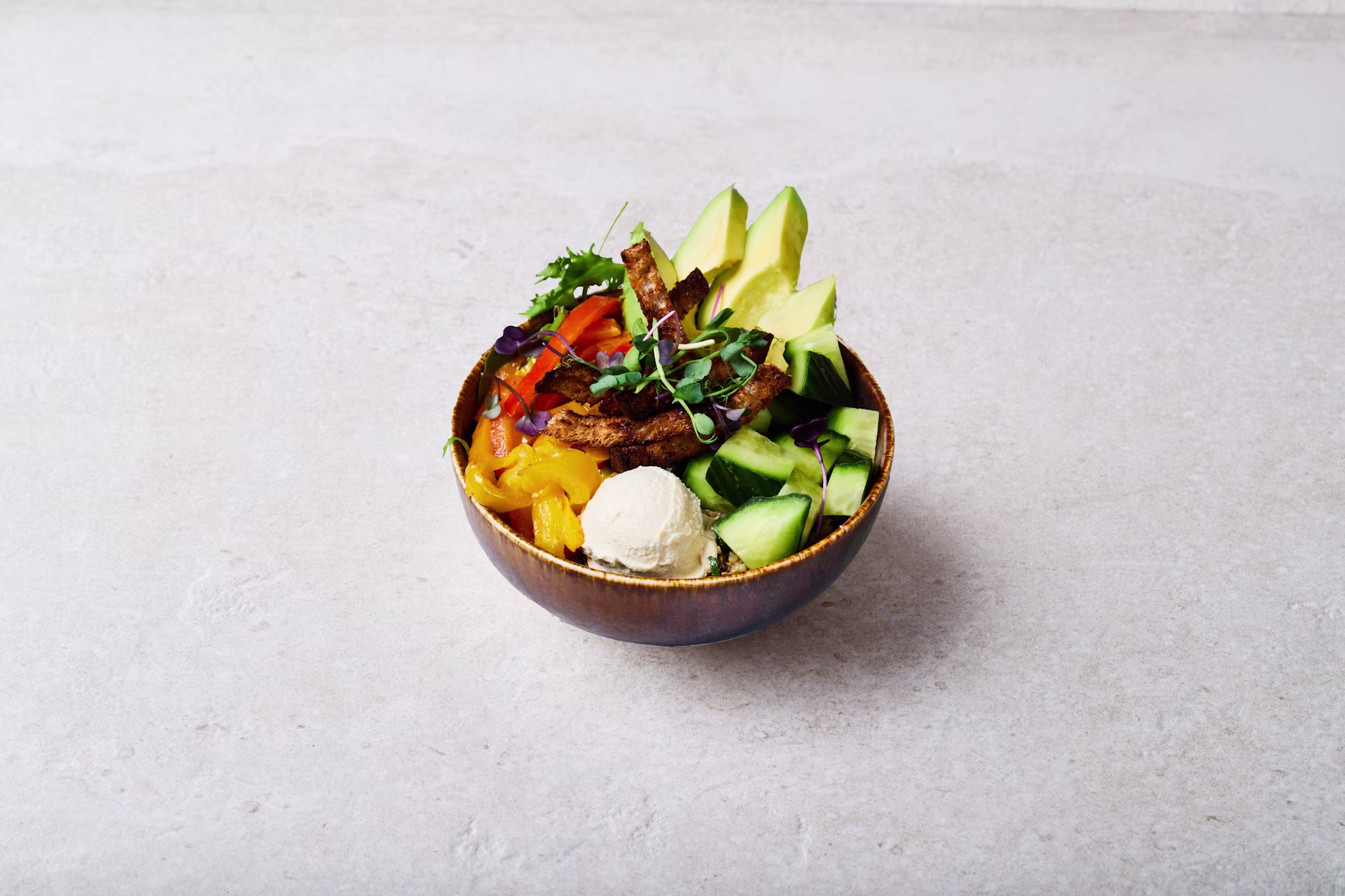 A close up picture of the seasonal vegetables bowl, a bowl with roasted peppers, avocado, quinoa tabbouleh, hummus, cucumber, mesclun, vegan vinaigrette, sprouted cress & homemade organic croutons